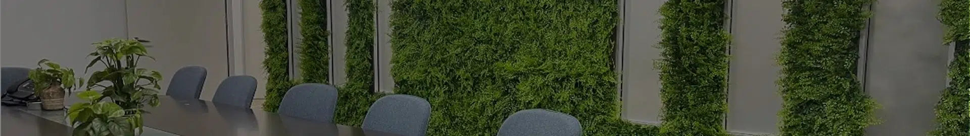 A long conference table with gray chairs in front of a wall covered in vertical green plants.