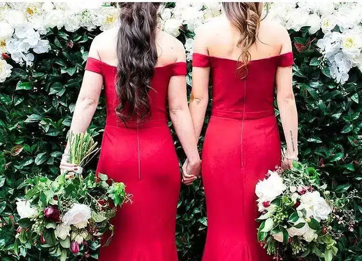 Two women in red off-shoulder dresses holding hands with floral bouquets against a green and white floral background.