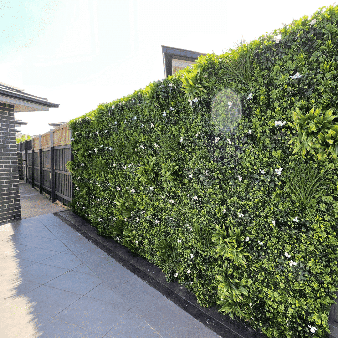 Green artificial hedge along a sidewalk with a building in the background