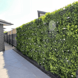 Green artificial hedge along a sidewalk with a building in the background
