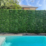 Artificial green wall with white flowers next to a pool