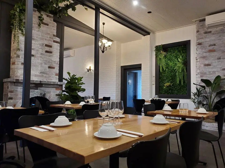 Modern restaurant interior with wooden tables, chairs, and decorative plants.