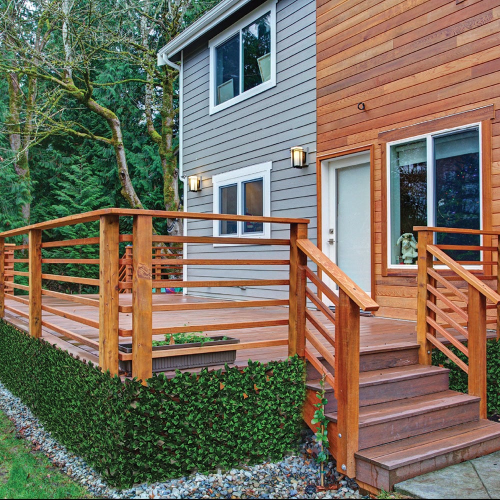 Wooden deck and stairs leading to a house with greenery in the background