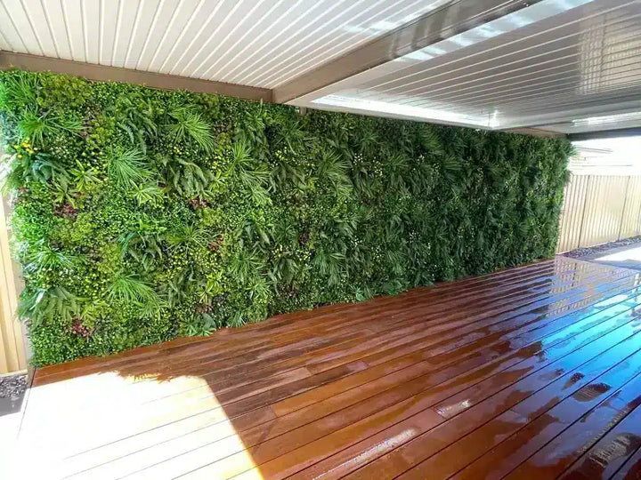A lush green vertical garden wall with dense tropical foliage, situated under a corrugated metal roof on a wet wooden deck.
