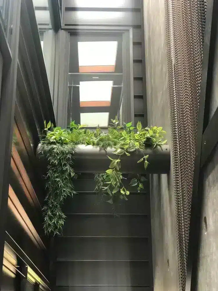 A modern dark gray staircase with a horizontal planter box filled with green trailing plants, set against a minimalist interior with wood and concrete walls.