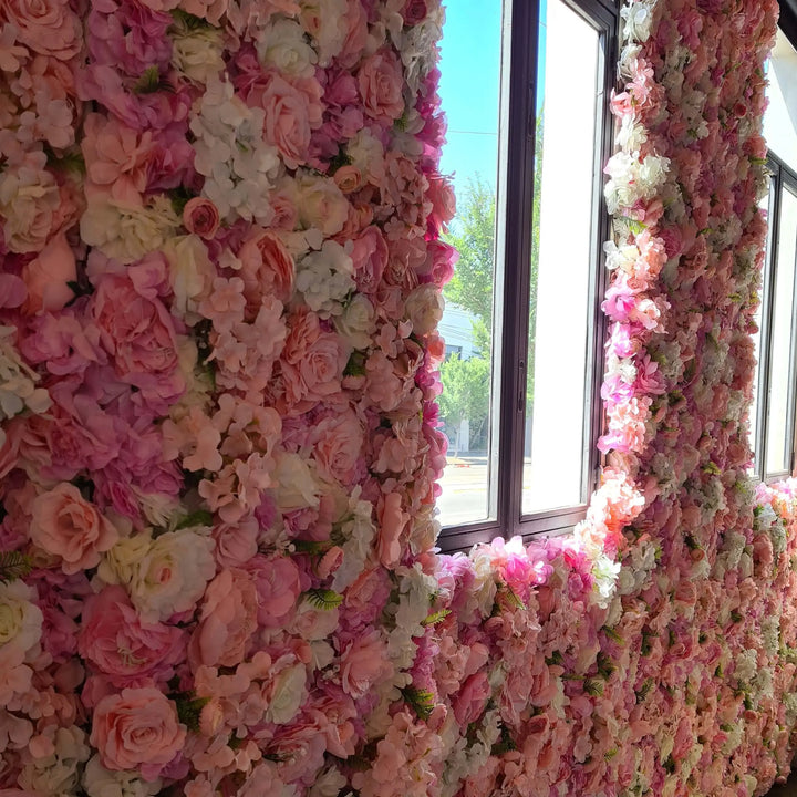 A large decorative wall covered in dense pink, blush, and white faux flowers, installed around window frames in an indoor setting.