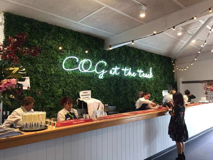 Neon sign 'COG at the trunk' above a counter with people in a modern interior setting.