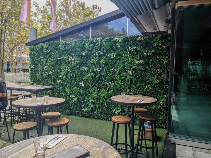 Outdoor seating area with tables and chairs near a green wall.