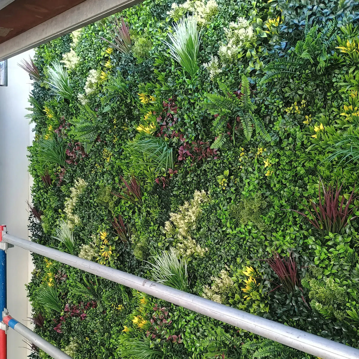 Artificial green wall panel with mixed foliage, vertical garden for interior or exterior decor.