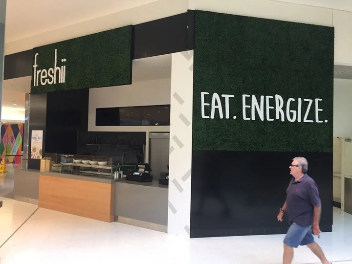 A storefront or cafe interior with a large dark green textured wall panel reading 'EAT. ENERGIZE.