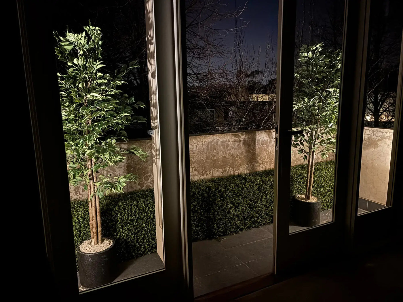 Very Beautiful Artificial Ficus Tree with UV Resistance 180cm, featuring lush green foliage and a natural-looking multi-stem trunk in a sleek black planter, displayed outdoors against a landscaped garden backdrop.