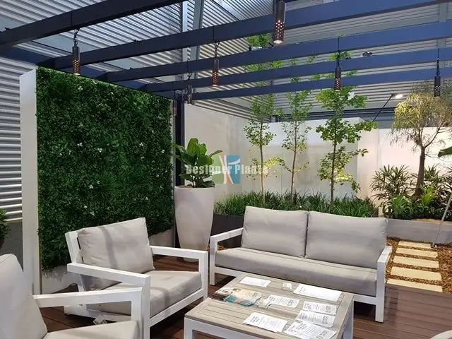 Outdoor patio furniture set including a white-framed sofa, two matching armchairs, and a rectangular coffee table with light wood tops, arranged under a blue pergola with a green living wall and potted plants in the background.