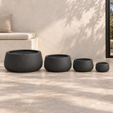 Four matt black soft-tapered bowl planters arranged on a covered terrace; sizes range from 20cm to 55cm diameter.