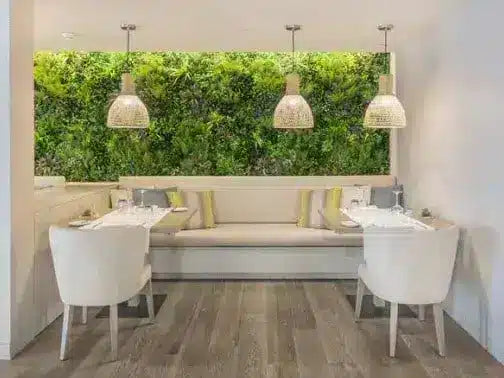 A modern dining nook with a built-in bench, two white chairs, three woven pendant lights, and a large green living wall backdrop.