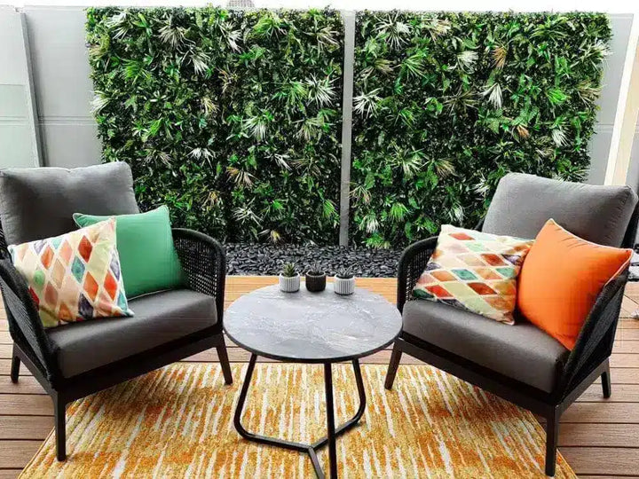Outdoor patio set with two chairs, a table, and colorful cushions against a green wall.