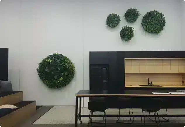 A modern interior space with a black kitchenette unit, a long table with black chairs, and several green spherical wall decorations mounted on a white wall.