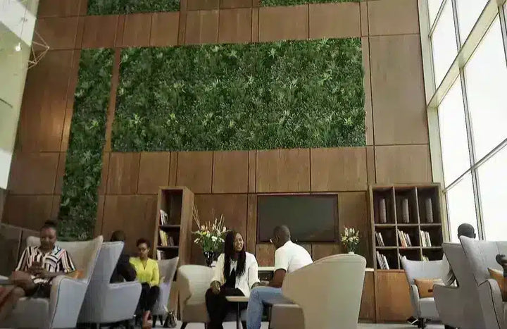 A high-angle view of a modern lounge area with people sitting and conversing in front of a large wood-paneled wall featuring a green living wall panel.