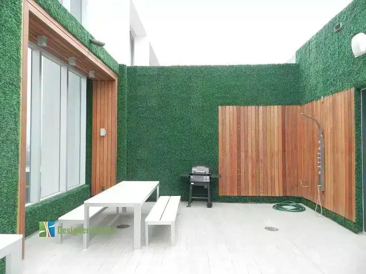 Outdoor patio area with green artificial grass walls, a white dining table and benches, a black grill, a wood-paneled wall, and a shower fixture.