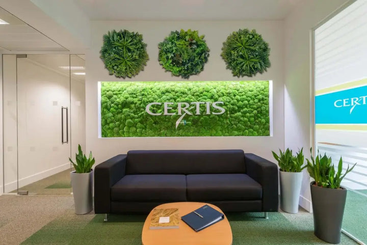 Modern office interior with a black sofa, coffee table, and green wall art displaying the Certis logo.