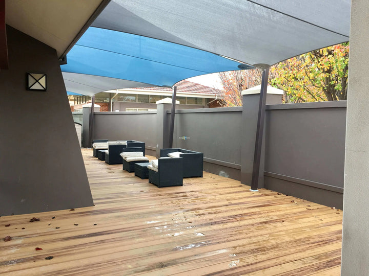 Outdoor patio area with a wooden deck, gray wall, blue canopy, and dark outdoor seating under a large gray awning.