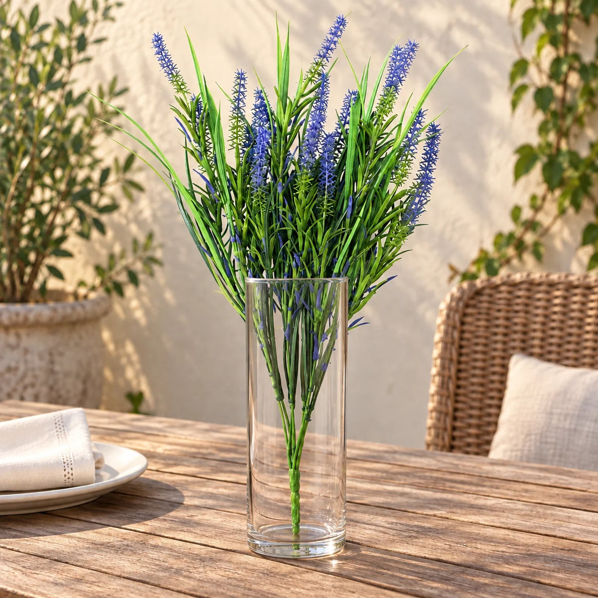 Purple artificial lavender stem in a clear vase on a sheltered outdoor dining table.