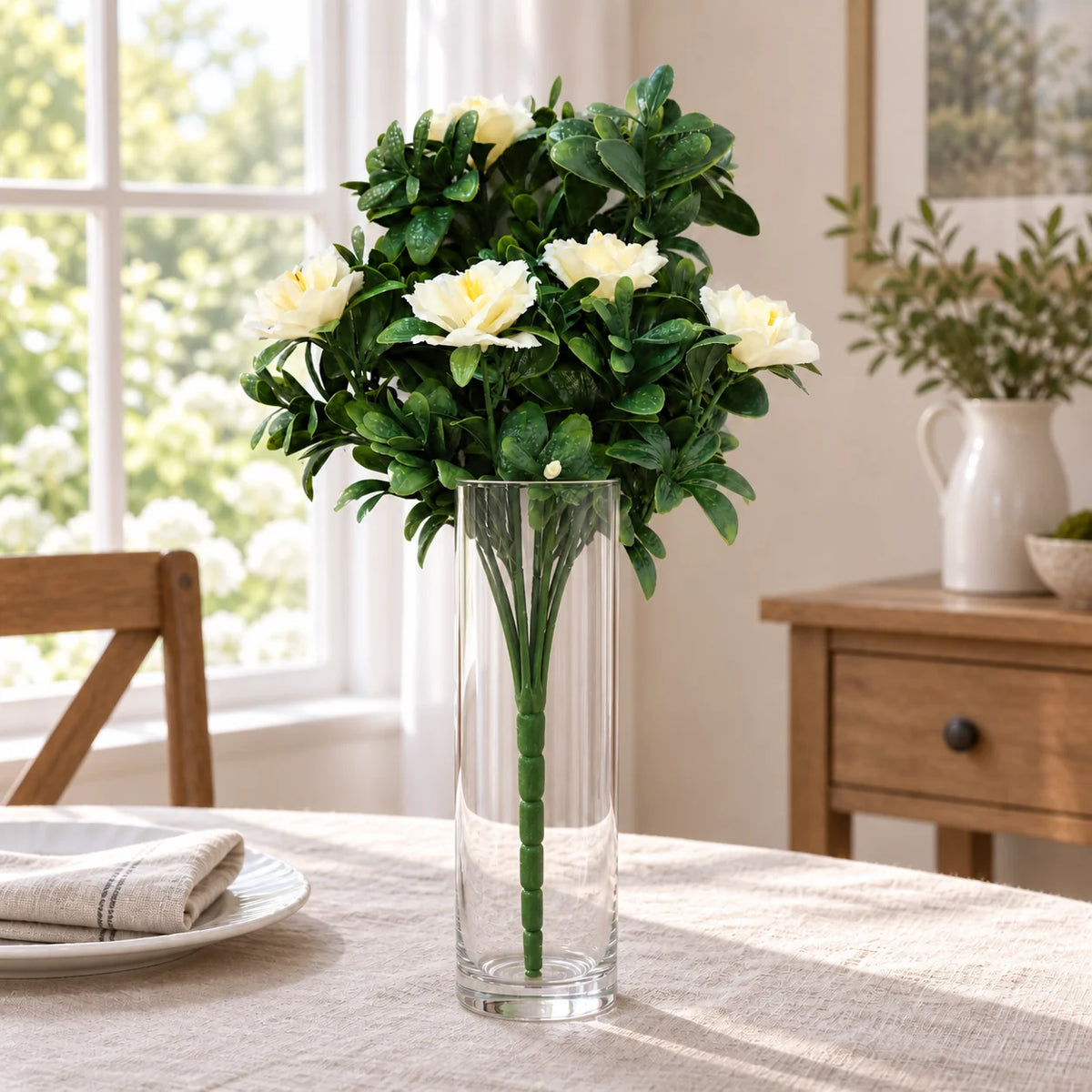 White artificial rose bunch in a clear vase on a linen-covered dining table.