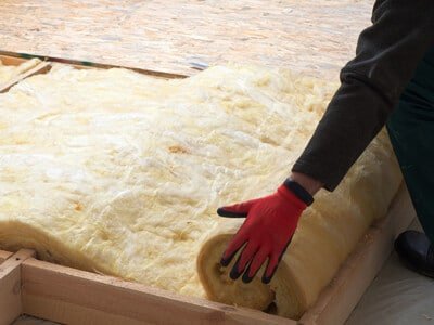 A person rolling out insulation in a home roof