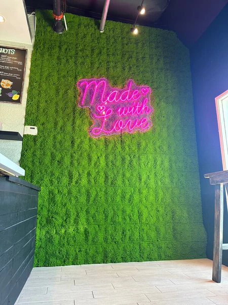 made with love neon company sign on top of faux moss wall